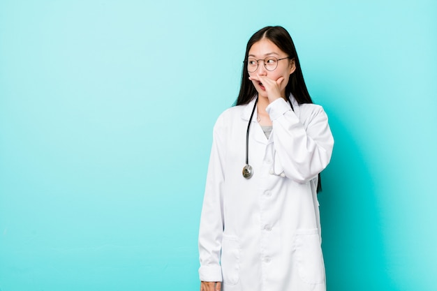 Mujer joven médico chino pensativo mirando a un espacio de copia que cubre la boca con la mano.