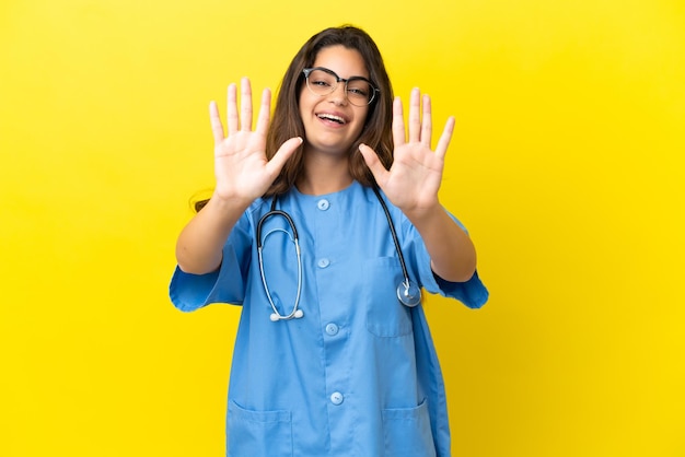 Mujer joven médico cirujano aislado sobre fondo amarillo contando diez con los dedos