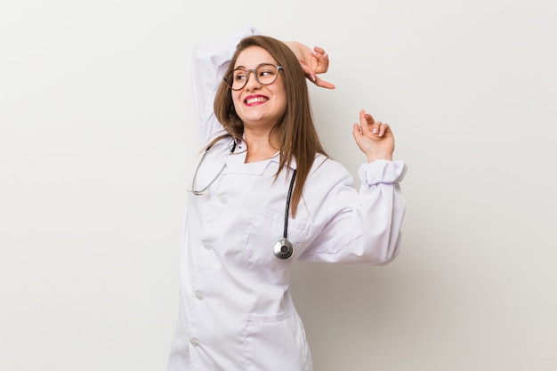 Mujer joven médico contra una pared blanca estirando los brazos, posición relajada.