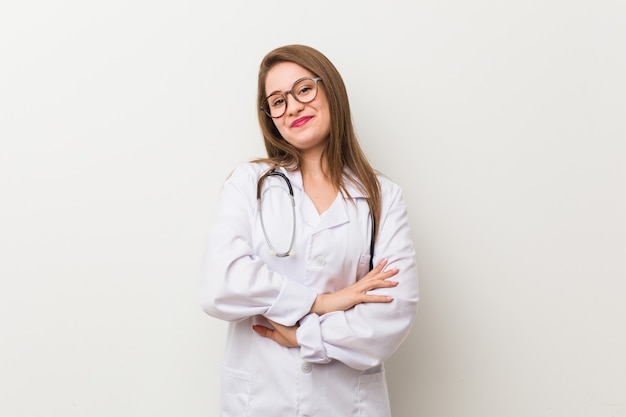 Mujer joven médico contra una pared blanca riendo y divirtiéndose.