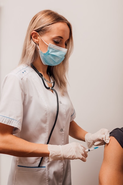 Mujer joven médico hace una inyección de vacunación al paciente en el brazo
