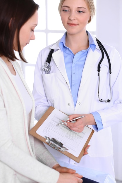 Mujer joven médico y paciente en examen médico en la oficina del hospital. Blusa de color azul de terapeuta se ve bien. Concepto de medicina y atención médica.