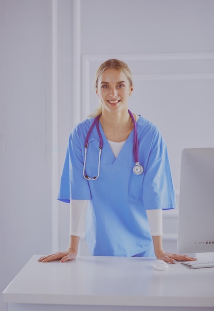 Mujer joven médico de pie junto a la mesa aislado sobre fondo blanco.