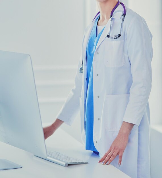 Mujer joven médico de pie junto a la mesa aislado sobre fondo blanco.