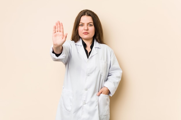 Mujer joven médico de pie con la mano extendida mostrando la señal de stop, previniéndote.