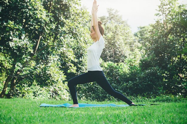 La mujer joven medita mientras que practica yoga en parque.