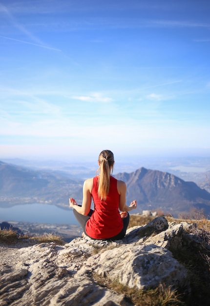 Una mujer joven meditando en la cima de la montaña.