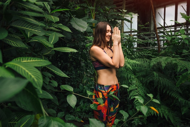 Foto mujer joven meditando mientras hace namaste gesto de la mano en invernadero