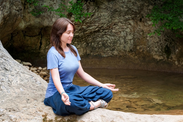 Mujer joven meditando en posición de loto cerca de waterfal