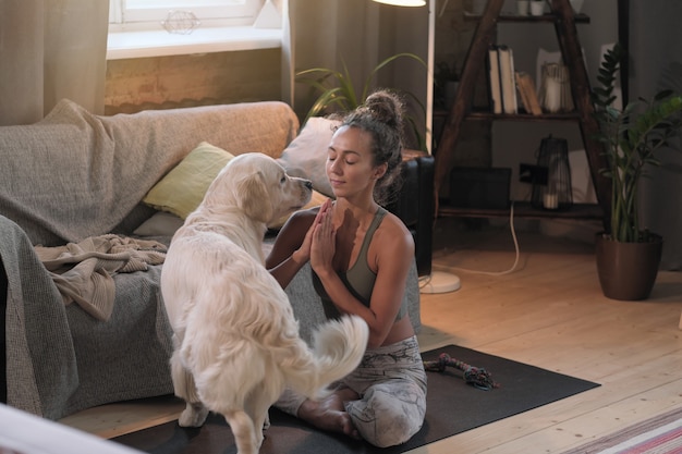 Mujer joven meditando en posición de loto en la habitación junto con su perro