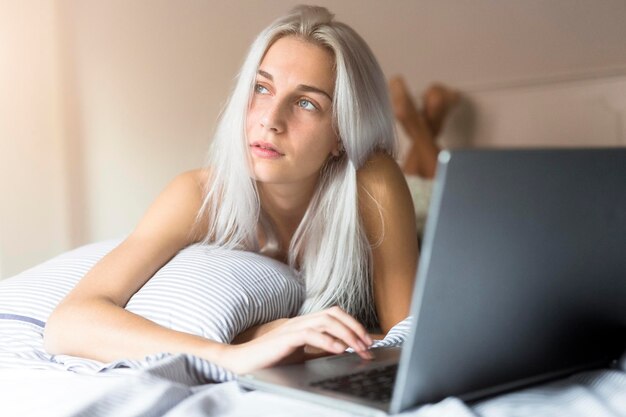 mujer joven, mentira en cama, usar la computadora portátil