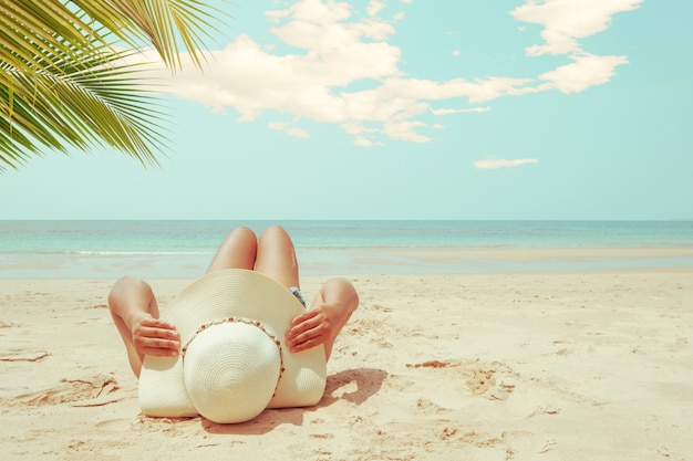 La mujer joven en la mentira del sombrero de paja toma el sol en una playa tropical