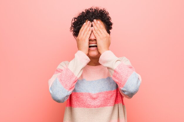 La mujer joven mezclada del adolescente afroamericano cubre los ojos con las manos, sonríe ampliamente esperando una sorpresa.