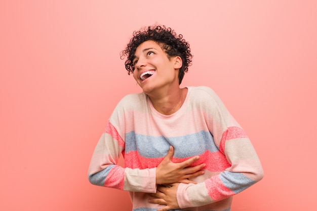 La mujer joven mezclada del adolescente del afroamericano ríe feliz y se divierte manteniendo las manos en el estómago.