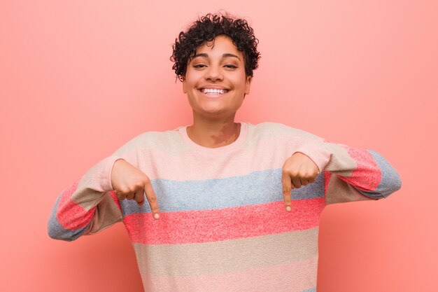 La mujer joven mezclada del adolescente del afroamericano señala hacia abajo con los dedos, sensación positiva.