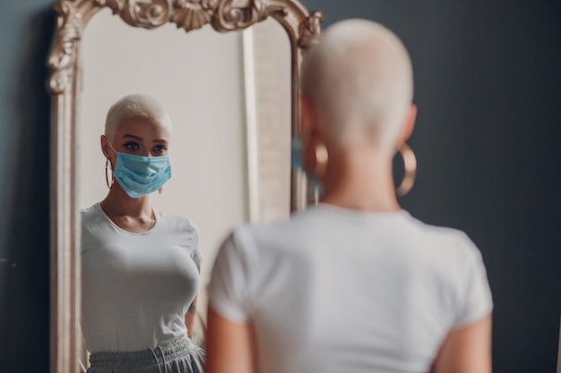 Mujer joven milenaria en mascarilla protectora médica con retrato de pelo rubio corto de pie en mi ...