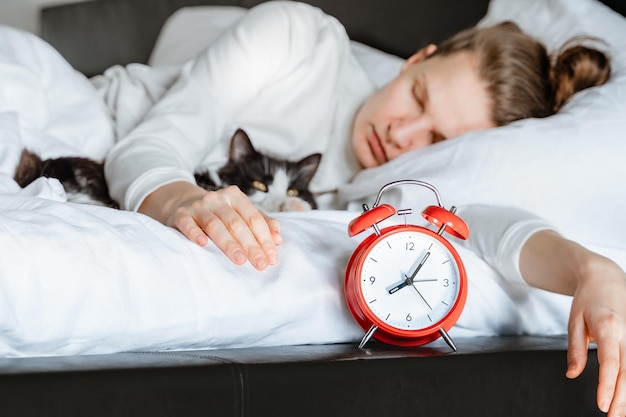 Mujer joven del milenio durmiendo con un gato mascota en una cama de manta blanca acogedora en casa despertador