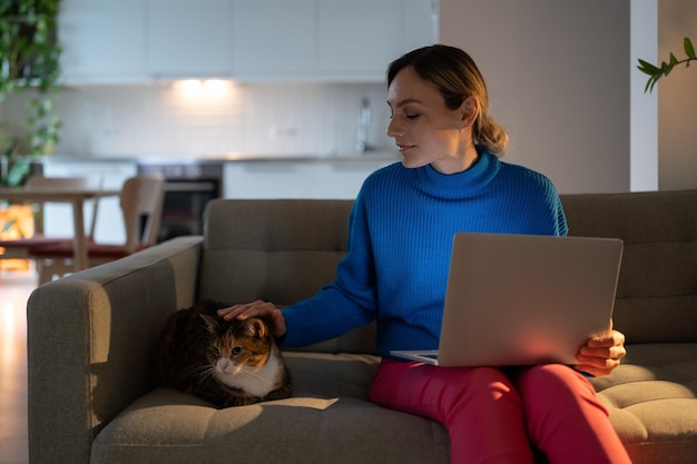 Mujer joven mira con expresión encantadora al gato doméstico y disfruta pasar tiempo con animales