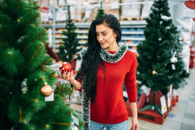 Mujer joven mira el juguete del árbol de Navidad en el supermercado.