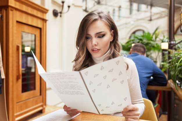 Mujer joven mira el menú en un café. Una hermosa rubia elige la comida en un hermoso restaurante.