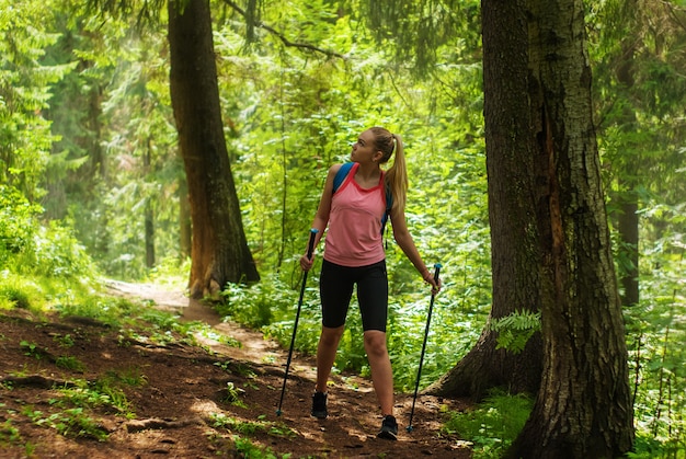 Mujer joven mira a su alrededor mientras camina por un sendero en un bosque de montaña