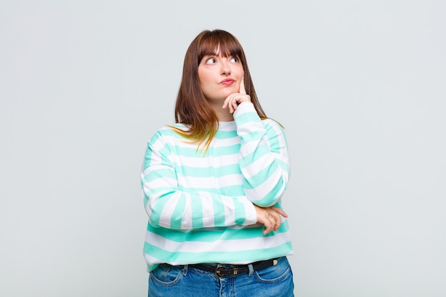 Mujer joven con mirada concentrada, preguntándose con expresión dudosa, mirando hacia arriba y hacia un lado