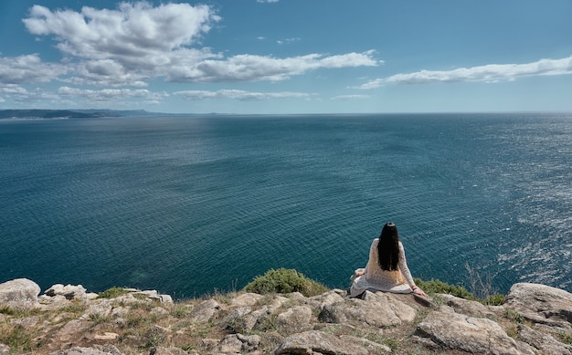 Mujer joven mirando al mar en un día soleado con nubes en el cielo desde lo alto de un acantilado