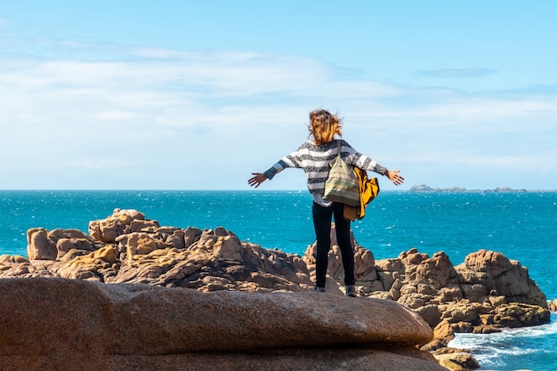 Una mujer joven mirando al mar a lo largo de Lighthouse Mean Ruz, puerto de Ploumanach, en la localidad de Perros-Guirec, Cotes-d'Armor, en la Bretaña francesa, Francia.