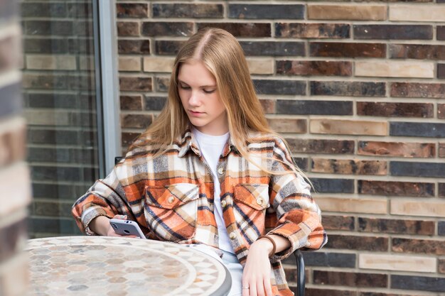 Mujer joven mirando algo en el teléfono mientras está sentada en una mesa de cafetería al aire libre