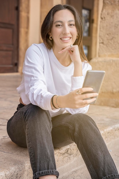 Mujer joven mirando a la cámara con la vida de la ciudad al aire libre de teléfono móvil
