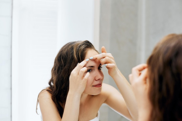 Mujer joven mirando y exprimiendo granos en la cara Cuidado de la piel