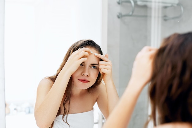 Mujer joven mirando y exprimiendo granos en la cara Cuidado de la piel