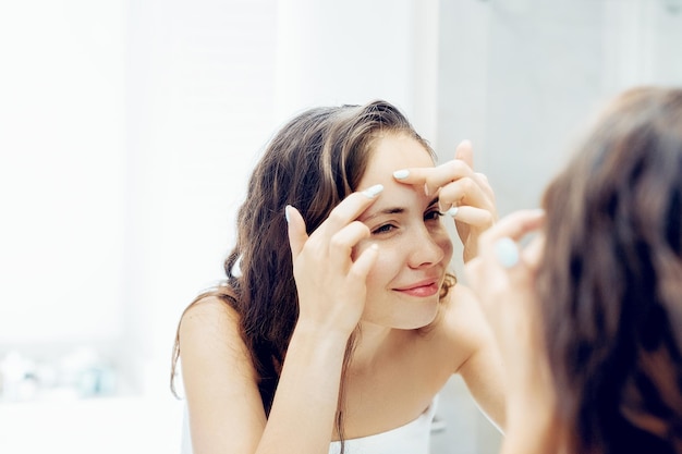 Mujer joven mirando y exprimir el acné en la cara frente al espejo. Chica fea con problemas de piel, chica adolescente con espinillas. Protección de la piel. Belleza