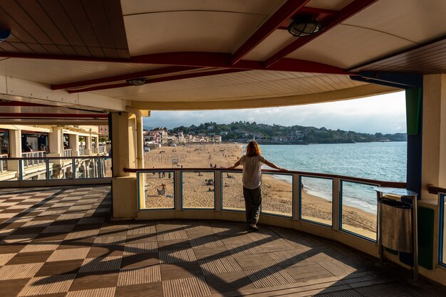 Una mujer joven mirando la hermosa Grande Plage en Saint Jean de Luz al atardecer, vacaciones en el sur de Francia, País Vasco francés