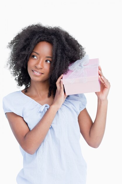 Mujer joven mirando a un lado mientras agita un regalo