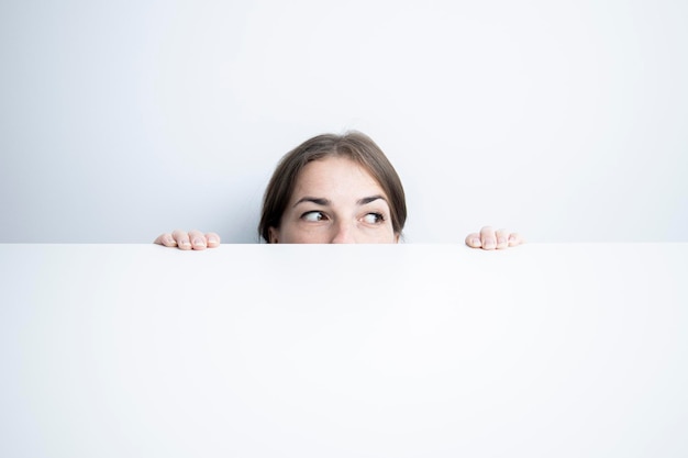 Mujer joven mirando hacia un lado mirando desde debajo de una mesa blanca contra una pared blanca