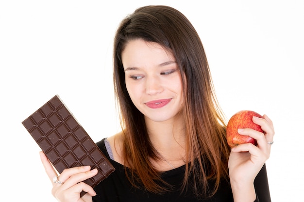 Mujer joven mirando manzana fresca mientras se come barra de chocolate