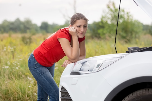 Mujer joven mirando el motor del coche roto en caminos rurales