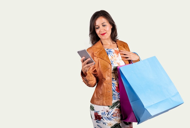 Mujer joven mirando el móvil y con algunas bolsas de la compra sobre un fondo blanco.