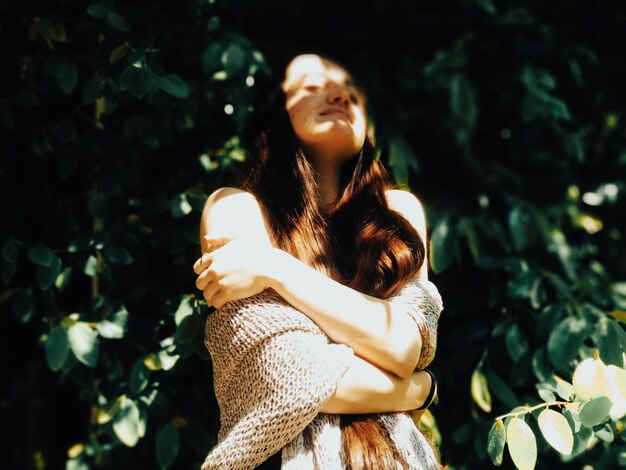 Foto mujer joven mirando hacia otro lado mientras está de pie en el árbol