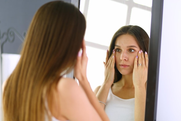 Mujer joven mirando a sí misma reflejo en el espejo en casa