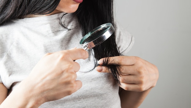 Mujer joven mirando su cabello con una lupa