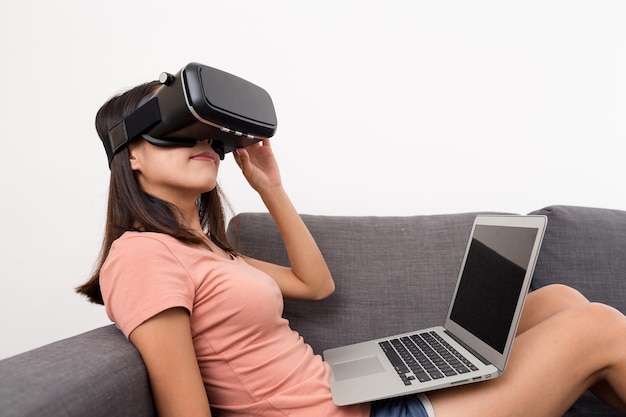 Mujer joven mirando a través de la realidad virtual con una computadora portátil en casa