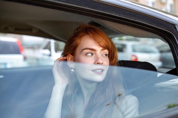 Mujer joven mirando por la ventanilla del coche Mujer joven en el asiento trasero de un coche mirando por la ventana