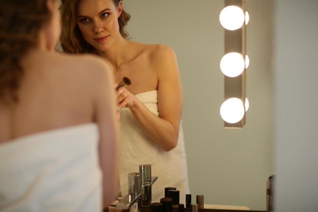 Mujer joven mirándose al espejo y maquillándose