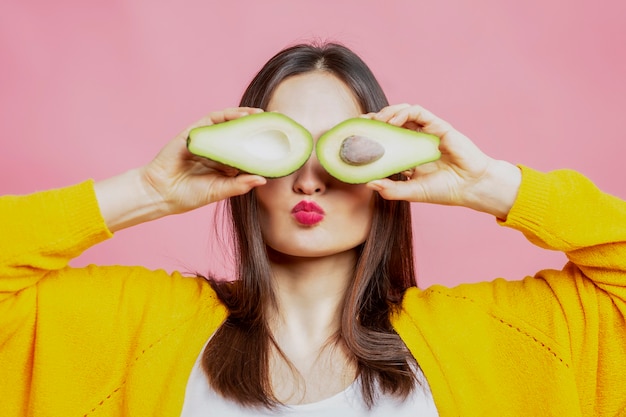 Mujer joven con mitades de aguacate. Hermosa morena con un suéter amarillo. Alimentación saludable y vegetarianismo.