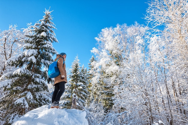 Mujer joven con mochila azul senderismo en bosque de invierno