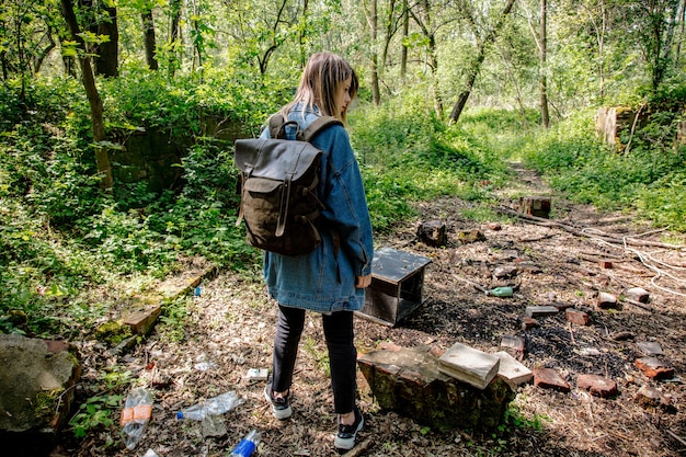 Mujer joven con mochila cerca de la basura en un bosque mixto Beskidy en Polonia en primavera.