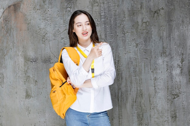 Mujer joven con mochila de pie sobre una pared gris. foto de alta calidad