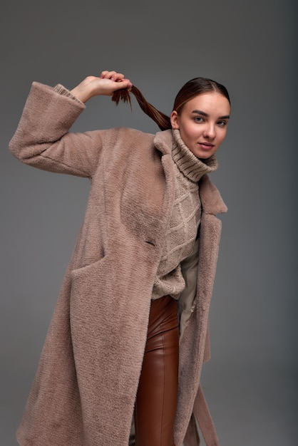 Mujer joven de moda en un abrigo de piel sintética sobre un fondo gris